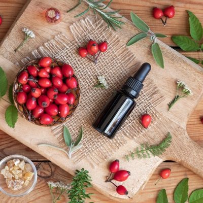 Homemade Rose Hip Oil Puffy Eye Serum in Amber Glass Bottle Surrounded by Rose Hips and Herbs | Vitacost.com/Blog