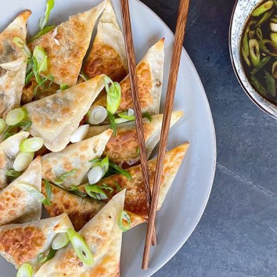 A Plate of Crispy, Triangular Dumplings With Wooden Chopsticks Sits Beside a Small Bowl of Sesame Scallion Dipping Sauce to Represent a Vegan Dumpling Recipe | Vitacost.com/Blog