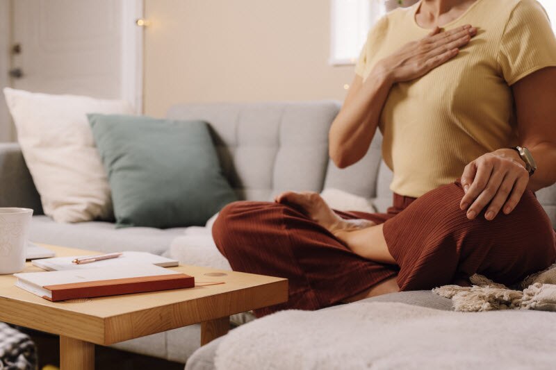 Stress and Heart Health Represented by Woman With Hand Over Chest on Couch | Vitacost.com/blog