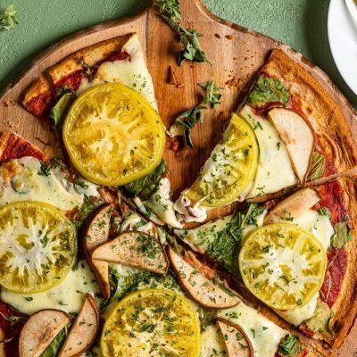 A Green Pizza With Green Tomatoes, Pears, Kale and Spinach Sit on a Wooden Pizza Peel | Vitacost.com/Blog