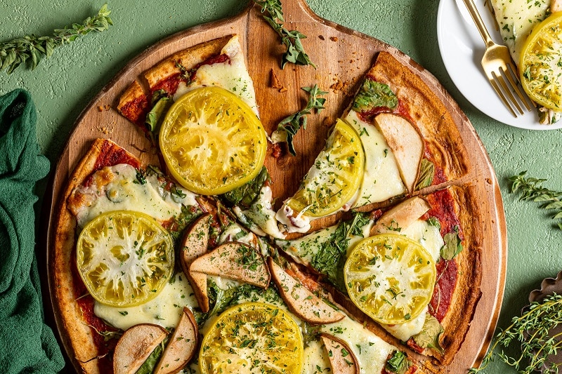 A Green Pizza With Green Tomatoes, Pears, Kale and Spinach Sit on a Wooden Pizza Peel | Vitacost.com/Blog