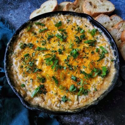 Cajun hot crab dip in cast iron skillet with melted dairy-free cheese and green onion, shown on dark blue tablecloth | Vitacost.com/blog