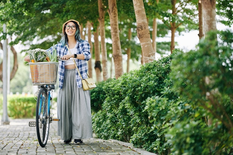 Woman Pushing Bicycle on Sidewalk with Basket Filled with Farmer's Market Goodies | Vitacost.ccom/Blog