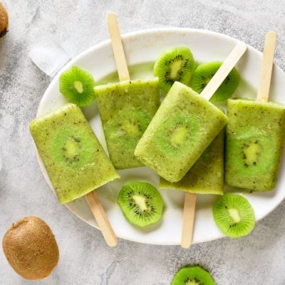 Kiwi fruit ice pops on wooden sticks on white plate with whole kiwis on the side | Vitacost.com/blog