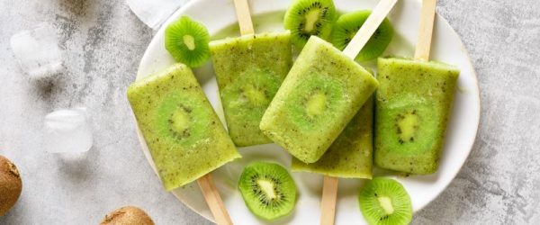 Kiwi fruit ice pops on wooden sticks on white plate with whole kiwis on the side | Vitacost.com/blog