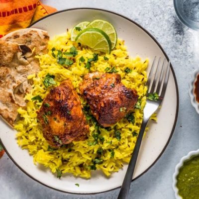 Tandoori chicken on yellow rice with naan on stoneware plate with bowls of sauce and colorful napkin | Vitacost.com/blog