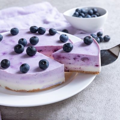 A Vegan Cheesecake Recipe With a Light Purple Blueberry Layer Topped With Fresh Blueberries Sits on a White Plate | Vitacost.com/Blog