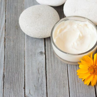 All-natural DIY hemorrhoid cream in glass jar on tabletop with flower and rocks next to it | Vitacost.com/blog