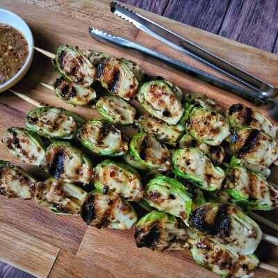 Maple-Mustard Grilled Brussels Sprouts on Skewers on Wooden Cutting Board with Sauce in a Bowl to the Side | Vitacost.com/blog