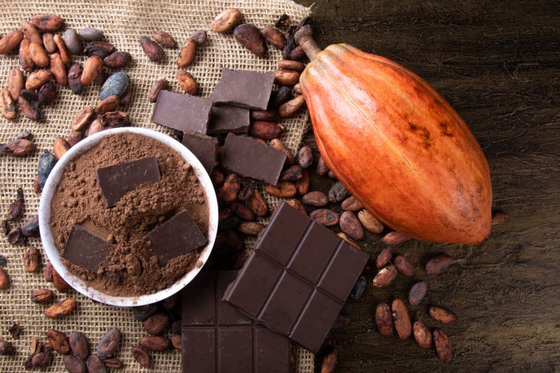 Benefits of Dark Chocolate for Men (Plus, Unique Bars to Try!) Benefits of Dark Chocolate for Men Represented by Overhead View of Cacao Beans, Pod, Power and Bars on Burlap and Wood Surface | Vitacost.com/blog