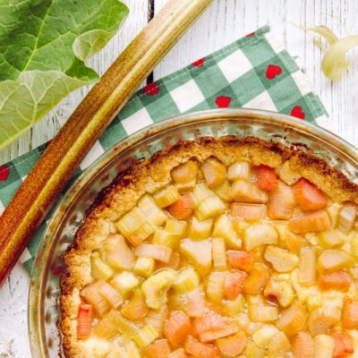 Gluten-Free Rhubarb Pie in Pie Plate on Checkered Napkin with Hearts on It Next to Stalk and Leaf of Rhubarb | Vitacost.com/Blog