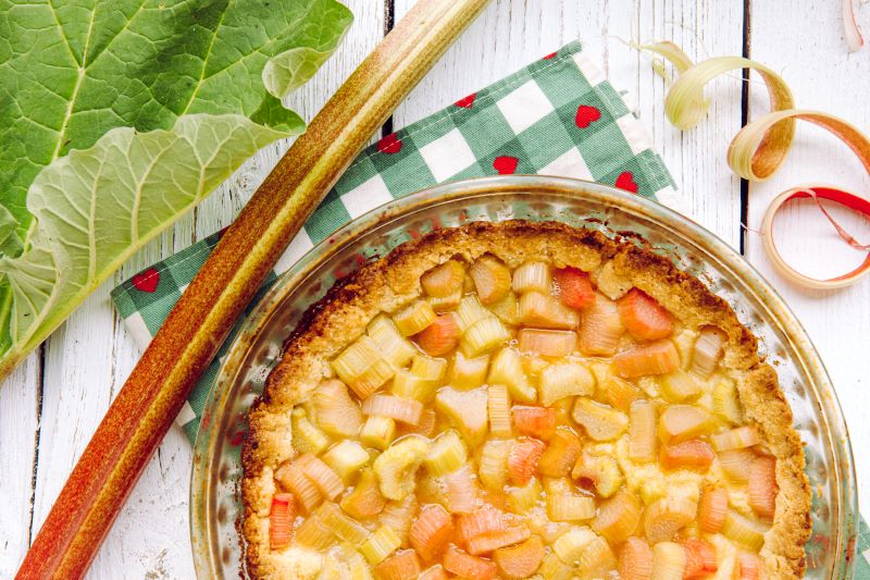 Gluten-Free Rhubarb Pie in Pie Plate on Checkered Napkin with Hearts on It Next to Stalk and Leaf of Rhubarb | Vitacost.com/Blog