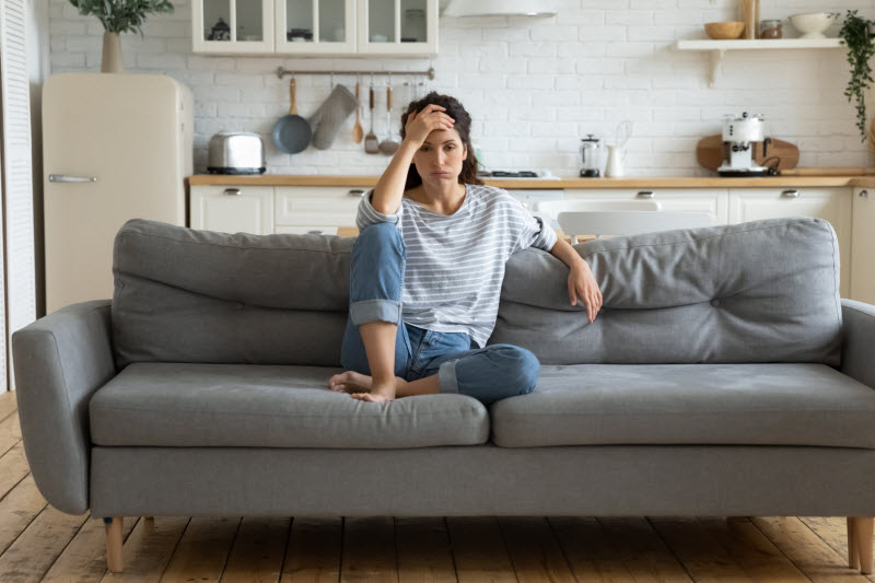 Woman Struggling With Inflammation and Mood Slumped on Couch with Frustrated Expression | Vitacost.com/blog
