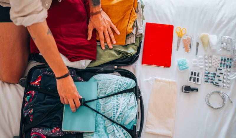Travel Probiotics: How They Work & What to Choose Person Packing Travel Probiotics & Other Trip Essentials into Suitcase on Bed | Vitacost.com/blog