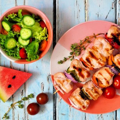 A Small Red Plate Has Two Skewers of Chicken Shish Kebabs With a Small Bowl of Salad and a Wedge of Watermelon | Vitacost.com/Blog