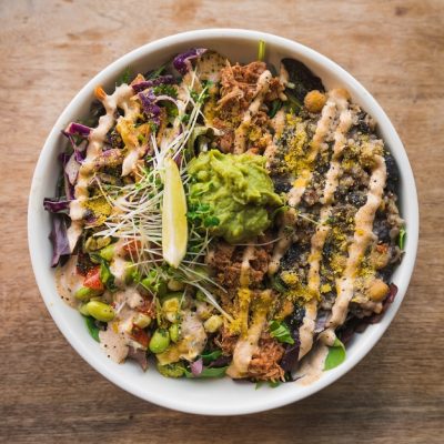 An Overhead Shot Shows a White Bowl Filled to the Brim With Vegan Burrito Bowl Ingredients and Topped With a Lime Wedge, Guacamole and Sprouts | Vitacost.com/Blog