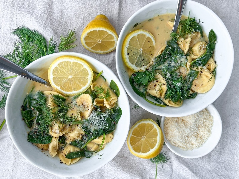 Two White Soup Bowls are Filled With a Lemon Tortellini Soup Recipe, Filled With Fresh Dill, Lemon Slices and Tortellini | Vitacost.com/Blog