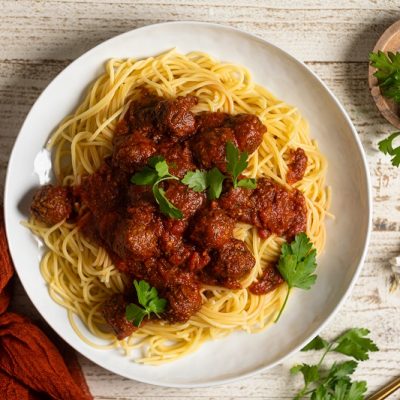 A Large White Plate Holds a Heaping Helping of Spaghetti With Saucy Meatballs and Parsley Sprigs, Representing a Vegan Meatball Recipe.