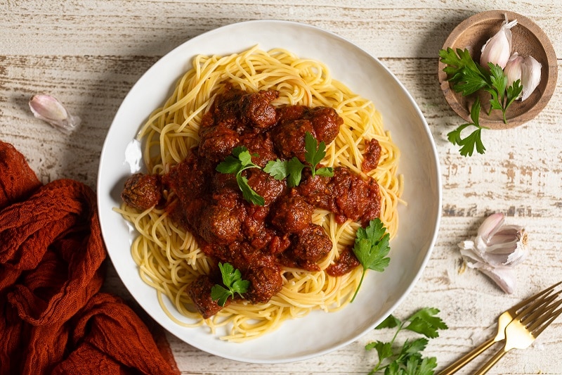 A Large White Plate Holds a Heaping Helping of Spaghetti With Saucy Meatballs and Parsley Sprigs, Representing a Vegan Meatball Recipe.