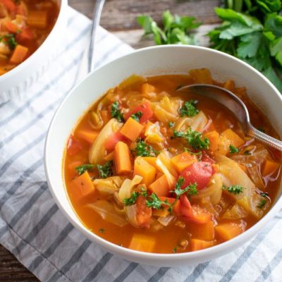 Vegetable Summer Soup with Fusilli Pasta in White Bowl on Counter with Striped Napkin