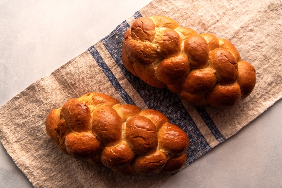 Two Braided Challahs Sit on a Dish Towel, Representing a Challah Recipe.