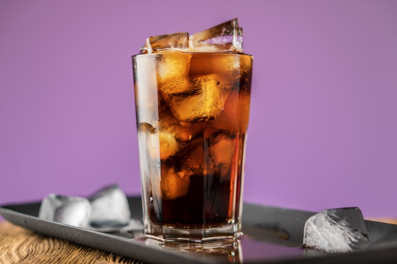 Healthy Soda in Glass Filled With Ice on Black Tray with Purple Background