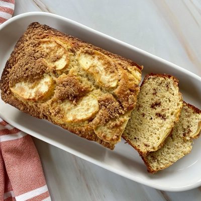 A Long White Serving Plate Displays an Apple Cinnamon Bread With a Few Slices Ready for the Taking.