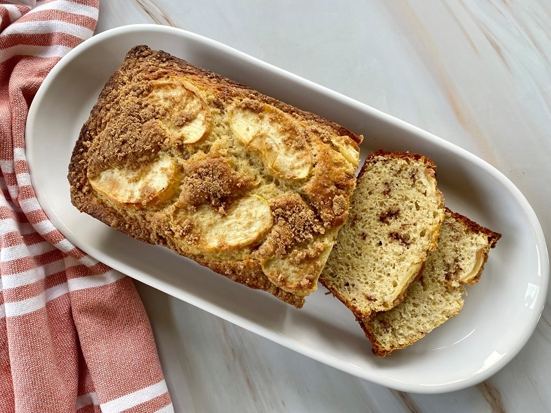 A Long White Serving Plate Displays an Apple Cinnamon Bread With a Few Slices Ready for the Taking.