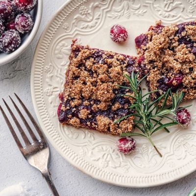 A Small, White Plate Has Two Cranberry Crumble Bars With a Sprig of Rosemary.