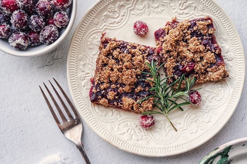 A Small, White Plate Has Two Cranberry Crumble Bars With a Sprig of Rosemary.