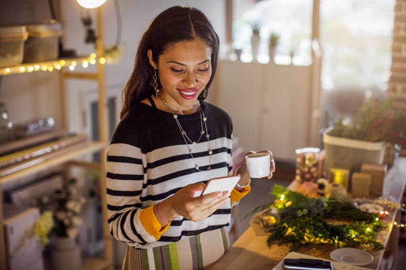 Woman Holiday Shopping on Phone in Kitchen Avoiding Financial Stress by Using Coping Techniques