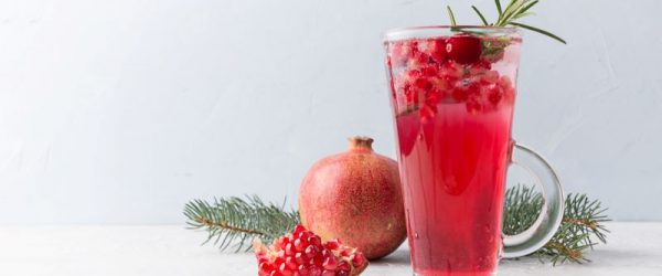 Pomegranate-Ginger Mocktail with Schisandra on Tall Glass Surrounded by Pomegranate & Greenery