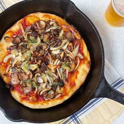 A Cast Iron Skillet Holds a Pizza With Mushrooms, Onions and Fennel to Represent a Cast Iron Skillet Pizza.