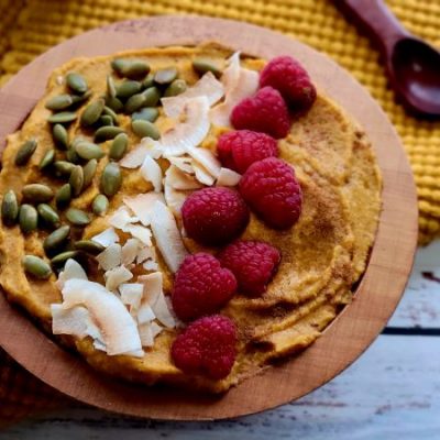 Sweet Potato and Collagen Smoothie Bowl Topped with Berries, Coconut Flakes and Pumpkin Seeds in Wooden Bowl on Textured Napkin