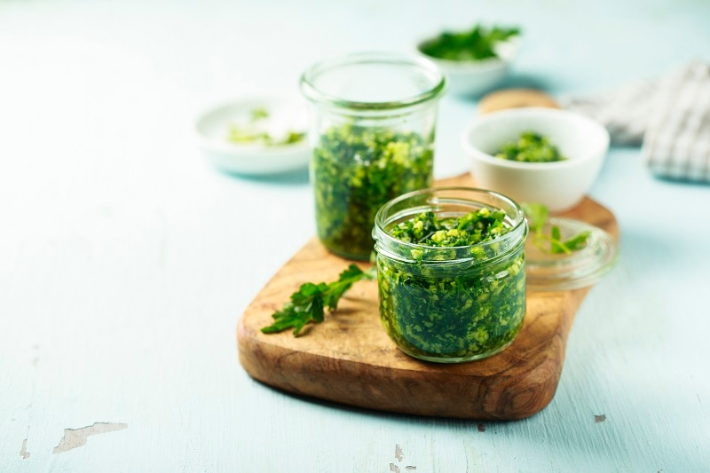 Two Jars of Homemade Parsley Pesto Sit on a Cutting Board.