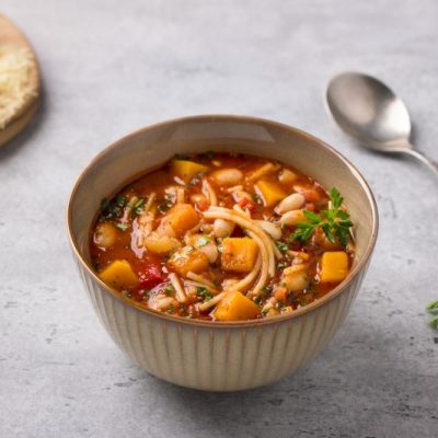 Pumpkin Minestrone Soup in Earthenware Bowl on Counter with Spoon & Bread
