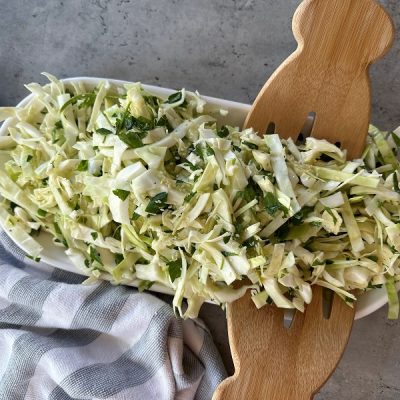 A Long Serving Bowl Holds a Cabbage Salad Recipe With Wooden Salad Servings Utensils.