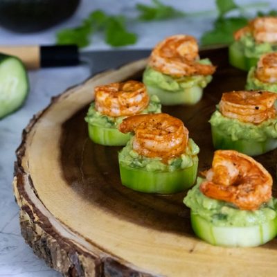 A Wooden Serving Platter Holds Shrimp Appetizers With Avocado Mash Over Cucumber Slices.