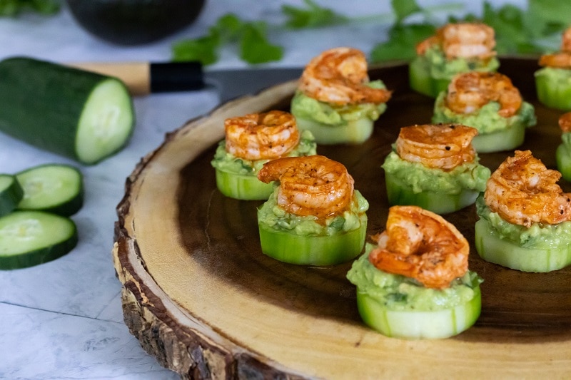 A Wooden Serving Platter Holds Shrimp Appetizers With Avocado Mash Over Cucumber Slices.