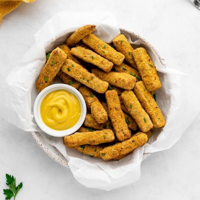 A White Serving Bowl is Lined With Paper and Filled With Air Fryer Tofu Fries With Yellow Dipping Sauce.