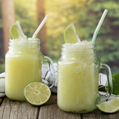 Brazilian Lemonade is Served in Large Glass Mugs Beside Limes in an Outdoor Setting.