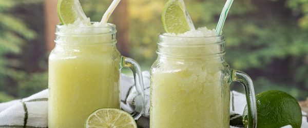 Brazilian Lemonade is Served in Large Glass Mugs Beside Limes in an Outdoor Setting.