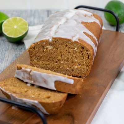A Coconut Bread With Key Lime Glaze Sits on a Long Wooden Platter Surrounded by Key Limes.