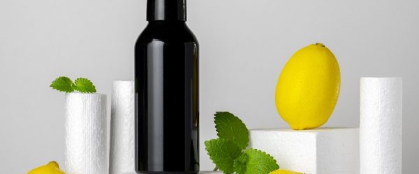 A Black Spray Bottle Sits on a White Platform Beside Lemons and Mint Sprigs, Representing Lemon as Deodorant.