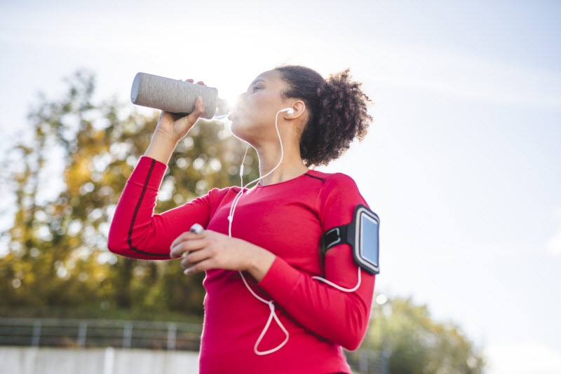 Woman Stopping Run to Drink from Water Bottle Heeding Signs and Symptoms of Dehydration