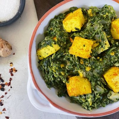 A White Ceramic Bowl With a Red Rim Shows Vegan Saag Paneer Using Tofu Instead of Cheese.