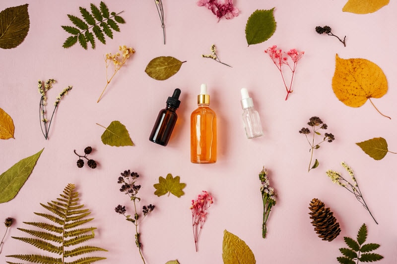 Natural Products on Pink Background Surrounded by Botanical Skincare Ingredients like Flowers and Leaves