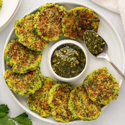 A Round Serving Plate Holds Zucchini Patties With a Green Sauce in the Center.