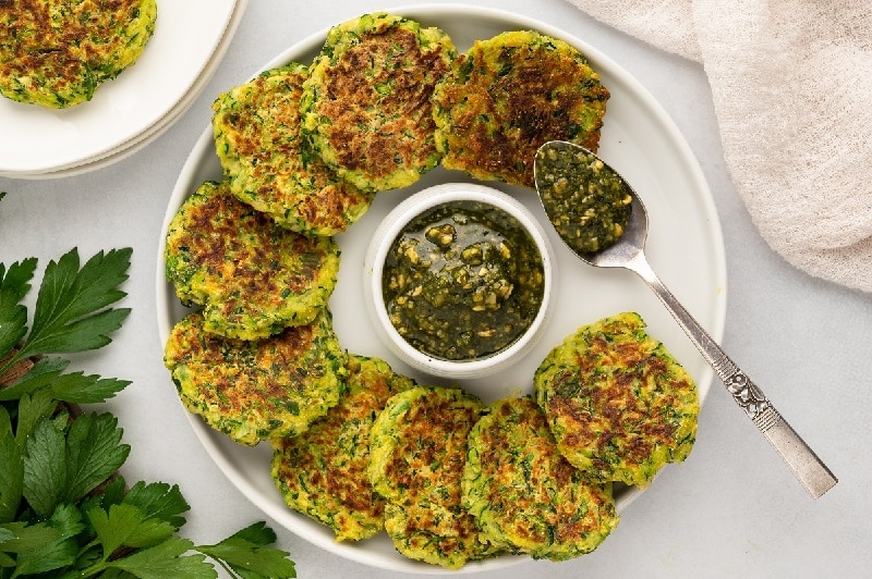 A Round Serving Plate Holds Zucchini Patties With a Green Sauce in the Center.
