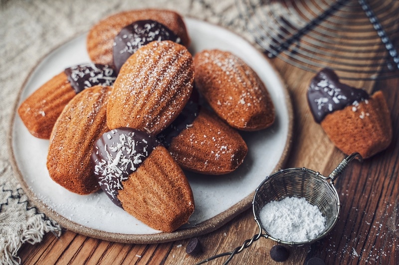 A Round White Plate is Covered With Chocolate-Dipped Gluten-Free Madeleines, Representing a Madeleine Recipe.